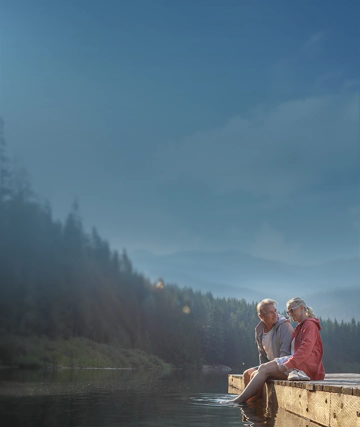 A woman and a man sitting on a dock at a lake